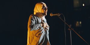 Eine kopftuchtragende Frau steht vor einem Mikrofon, schließt die Augen und hält eine Hand auf ihre Brust. Es ist Rabab Chamseddine