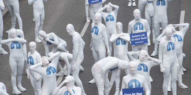 Demonstranten stehen in weißen Ganzkörperanzügen und blau aufgedruckten Lungensymbolen auf einer Straße