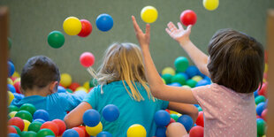 Drei Kinder, von hinten zu sehen, spielen in einem Bällebad