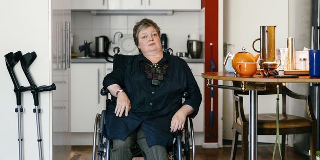 Eine Frau sitzt schief in einem Rollstuhl in ihrer Küche