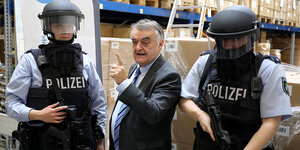 Herbert Reul (CDU, M), Nordrhein-Westfalens Innenminister, steht zwischen zwei Polizisten, die ballistische Schutzhelme tragen.
