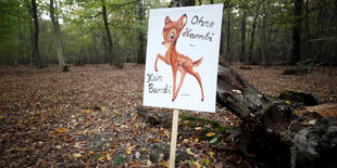 Ein Schild in einem Wald. Darauf steht „Ohne Hambi kein Bambi“. Außerdem ist ein Rehkitz darauf zu sehen