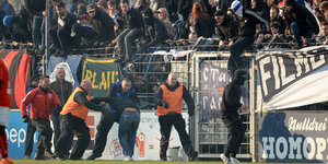 Fußball-Fans klettern über eine Absperrung zum Spielfeld.