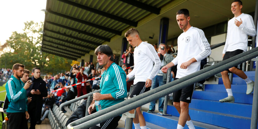 Nationalelf-Trainer Jogi Löw betritt mit seinen Spielern das Stadion auf dem Wufplatz in Berlin. Im Hintergrund jubeln Fans der Mannschaft zu.