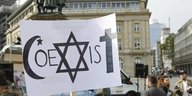 Auf einem Protestplakat bilden ein muslimisches, ein jüdisches und ein christliches Symbol den Schriftzug "Coexist"