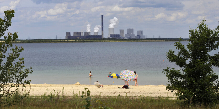 Ein Strand an einem See, der früher ein Tagebau war, dahinter ein großes Kraftwerk