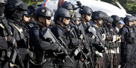 Schwarz gekleidete und behelmte Polizisten mit Maschinenpistolen stehen in einer Reihe