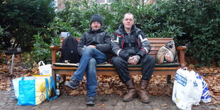 Zwei Obdachlose sitzen auf einer Parkbank.