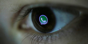 Ein menschliches braunes Auge, in dessen Pupille sich das grün-weiße WhatsApp Logo wiederspiegelt.