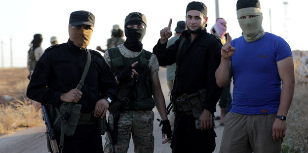 Vier junge Männer, teils mit Masken, stehen auf einer Straße in Syrien