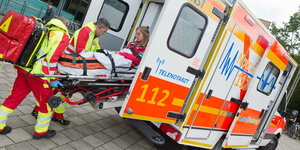 Rettungssanitäter schieben Bahre mit Patientin in Rettungswagen mit der Aufschrift 