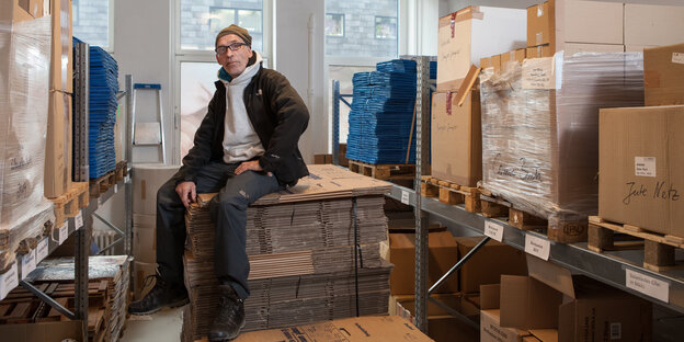Der Umzugsprofi Carlos Antoniazzi sitzt in einem Lagerraum auf einem Stappel gefalteter Kartons
