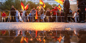 Demonstranten stehen mit Deutschlandflaggen vor einem Gitter, daneben Polizisten