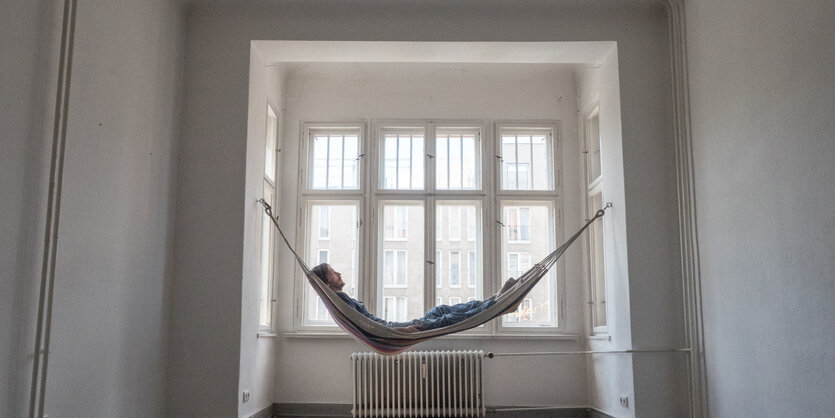 Ein leeres Zimmer, am Fenster eine Hängematte, darin liegt ein Mann