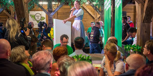 Eine Frau im Dirndl redet im Bierzelt, dahinter Grüne Parteiwerbung