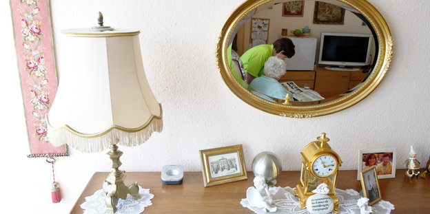 Kommode mit einer Lampe und einem Spiegel, in dem eine Pflegerin zu sehen ist