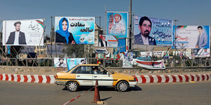Wahlplakate hängen an einer Straße, davor fährt ein Auto