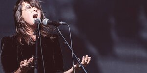 Eine Frau singt in eine Mikrofon, die Arme hält sie leicht gehoben