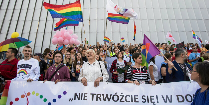 Viele Menschen mit bunten Fahnen stehen hinter einem Banner