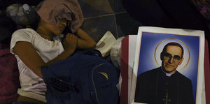 Eine Frau sitzt im Dunkeln auf dem Boden, neben sich ein Bild Oscar Romeros
