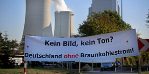 Banner mit der Aufschrift "Kein Bild, kein Ton. Deutschland ohne Braunkohlestrom" vor dem qualmenden Kraftwerk Neurath