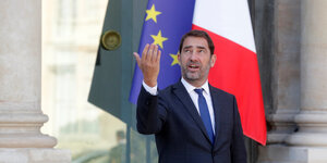 Christophe Castaner, der neue französische Innenminister, steht vor einer französischen und einer europäischen Flagge, blickt nach oben und hebt den angewinkelten rechten Arm wie zum Gruß