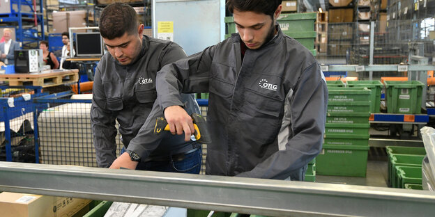Zwei junge Männer stehen in einer Fabrik, und einer hält eine Bohrmaschine