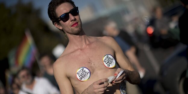 Ein Mann mit freiem Oberkörper hat runde Aufkleber auf den Brustwarzen. Darauf steht: Stop hatespeech