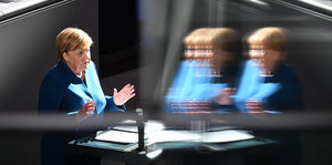 Angela Merkel steht im Plenum des Deutschen Bundestags und hebt beide Hände