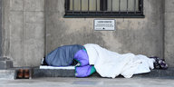 ein Mensch liegt in Schlafsäcke gehüllt auf der Straße