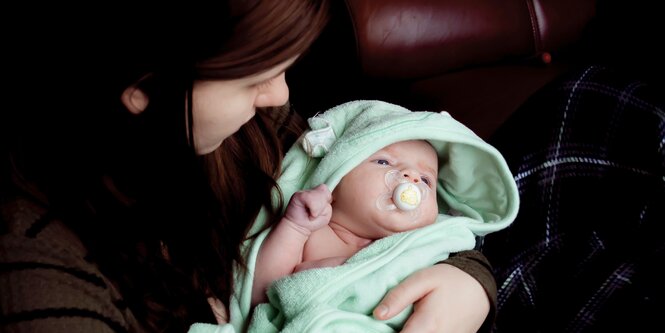 Eine Frau hält ein Baby, das in ein türkisfarbenes Handtuch gehüllt ist