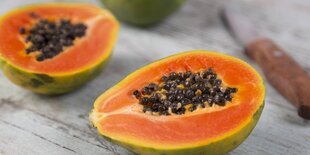 Eine aufgeschnittene Papaya liegt neben einem Messer auf einem Tisch