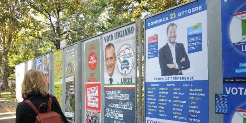 Eine blonde Frau mit Rucksack spaziert in einer Allee und schaut auf Wahlplakate.