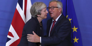 Ein Mann und eine Frau begrüßen sich mit Wangenküsschen, im Hintergrund die Flaggen von Großbritannien und der Europäischen Union