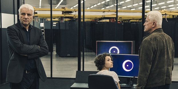 Zwei Männer stehen neben einer Frau, die vor einem Computerbildschirm sitzt