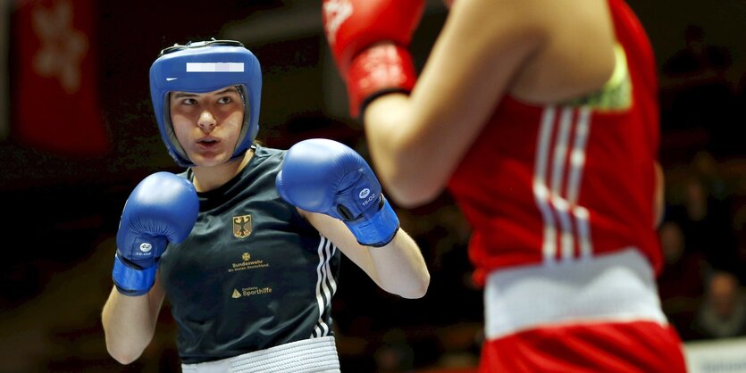 Eine Frau mit blauen Boxhandschuhen links kämpft gegen eine Frau mit roten Boxhandschuhen rechts.