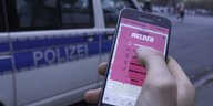 Ein Smartphone mit dem Eingabeformular der "Cop-Map" vor einem Polizeiauto