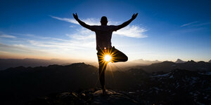 Yoga - Mensch in Yoga-Pose vor der tief stehenden Sonne