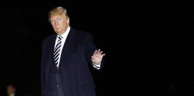 Donald Trump steht mit einem blauen Anzug bekleidet vor schwarzem Hintergrund.