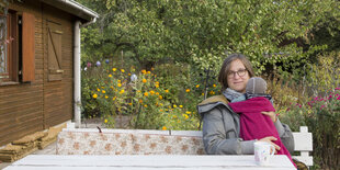 Frau mit Kind auf ihrem Arm auf einer Bank in einem Garten