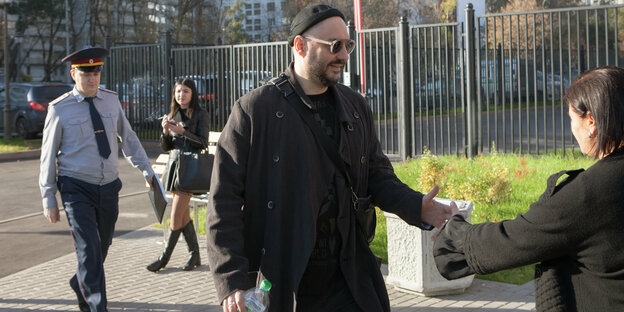Kirill Serebrennikow, ein Mann in schwarzer Kleidung und mit schwarzer Mütze und Sonnenbrille geht auf eine Frau zu und reicht ihr die Hand