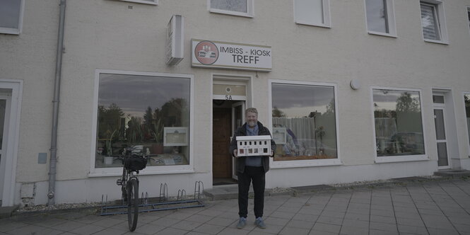 Georg Genoux steht vor einer Kneipe und trägt das Bühnenbild vor sich