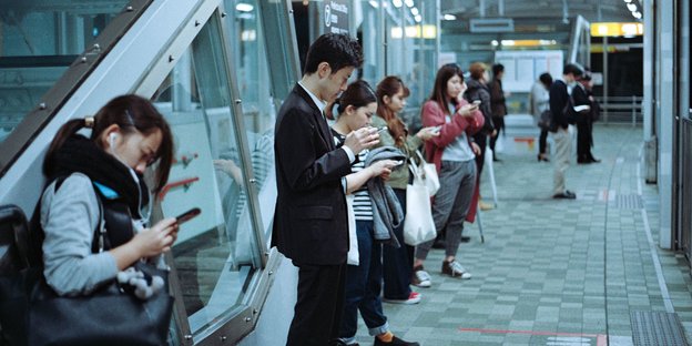 Menschen stehen auf einem Bahnsteig und gucken auf ihre Handys