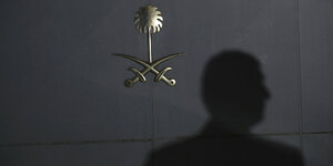 Schatten eines Menschen auf einer Tür mit saudischem Staatswappen