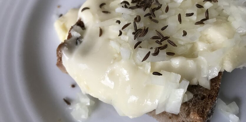 Eine hellgelbe Masse auf einem Brot, mit Kümmel bestreut