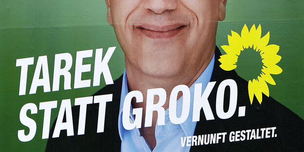 Auf einem grünen Plakat ist die untere Hälfte des Kopfes eines grinsenden Mannes zu sehen, quer darüber steht „Tarek statt Groko.“