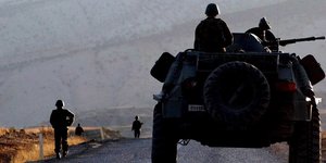 Ein Militärfahrzeug und ein Soldat auf einer Straße, im Hintergrund ein Berg.