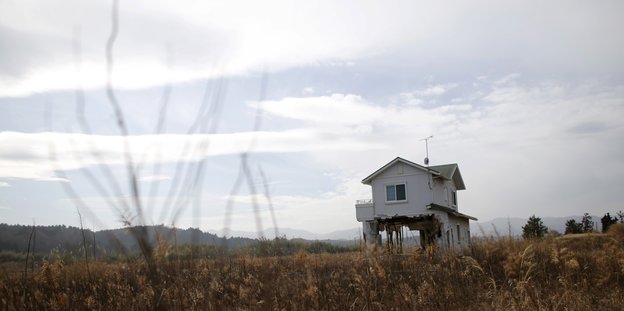 Ein Haus steht mitten in einer zerstörten Landschaft, der Himmel ist grau und bewölkt.
