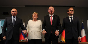 Putin, Merkel, Erdogan und Macron stehen nebeneinander und halten sich anden Händen