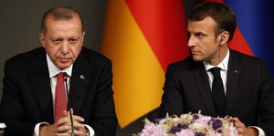 Erdogan sitzt neben Frankreichs Präsident Macron an einem Tisch mit Mikrofonen bei einer Pressekonferenz